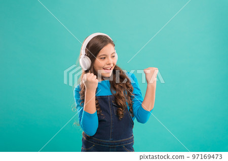 She isnt nothing but a winner. Happy little child making winner gesture on blue background. Small winner listening to music in headphones. Excited winner or champion celebrating victory 97169473
