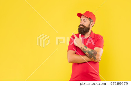Serious deliveryman in casual red cap and tshirt pointing finger aside copy space, advert Serious deliveryman in casual red cap and tshirt pointing finger aside copy space, advert 97169679