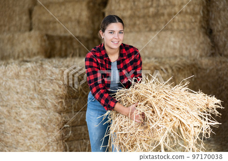 Young woman farmer standing with hay in her hands on farm 97170038