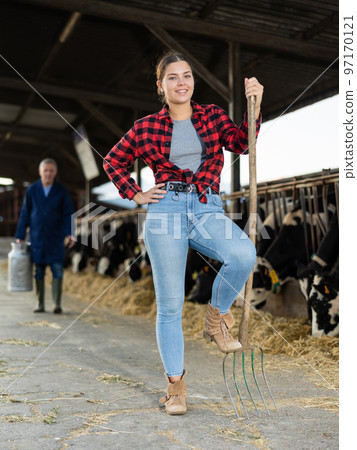 Full length portrait of girl farmer with pitchfork in outdoor cowshed 97170121