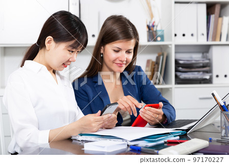 Two women write sms by phone in the office Two women write sms by phone in the office 97170227
