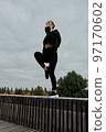 A woman in a black tracksuit does sports in the park 97170602