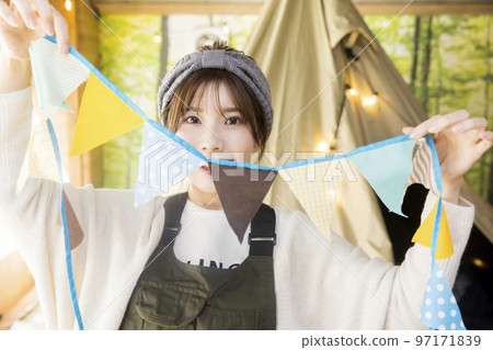 A young woman decorating with a garland at a house camp. A young woman decorating with a garland at a house camp. 97171839
