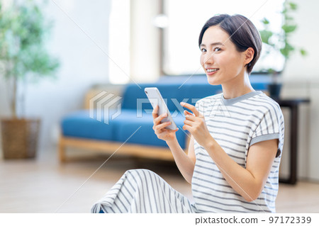 一位女士在客廳裡操作智能手機。 97172339