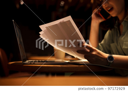 Young businesswoman holding paperwork while working and talking on phone at cafe. Young businesswoman holding paperwork while working and talking on phone at cafe. 97172929