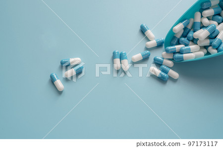 Blue-white capsule pills spread out of plastic spoon on blue background. Prescription drug. Healthcare and medicine. Tele pharmacy banner. Pharmaceutical product. Medical care. Pharmaceutical industry 97173117