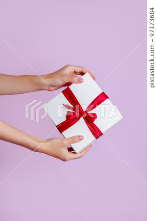 Women's hands hold a white with a red ribbon bow Women's hands hold a white with a red ribbon bow 97173684