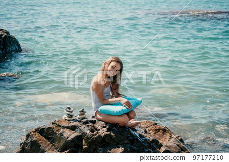 Woman with daughter bilds stones pyramid on seashore on a sunny day on the blue sea background. Happy family holidays. Pebble beach, calm sea. Concept of happy vacation on the sea, meditation, spa Woman with daughter bilds stones pyramid on seashore on a sunny day on the blue sea background. Happy family holidays. Pebble beach, calm sea. Concept of happy vacation on the sea, meditation, spa 97177210