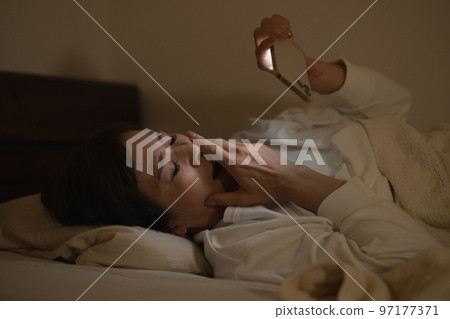 Woman getting sleepy looking at smartphone in bed Woman getting sleepy looking at smartphone in bed 97177371