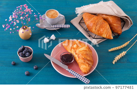 Tasty breakfast with croissants, fresh blueberries, jam and cup of coffee. Blue wooden table, high angle of view, no people. 97177481