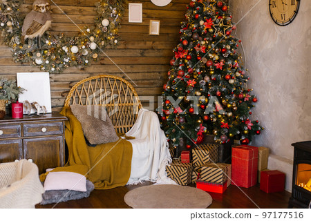 Christmas decor in the living room of a country wooden house with a traditional Christmas tree decorated with red and gold toys Christmas decor in the living room of a country wooden house with a traditional Christmas tree decorated with red and gold toys 97177516