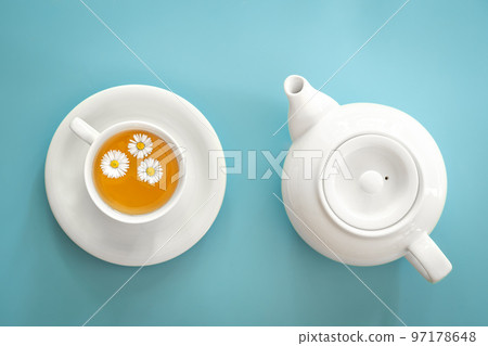 A cup of chamomile tea and a teapot on a blue background. A cup of chamomile tea and a teapot on a blue background. 97178648