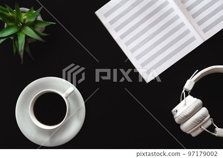 A cup of coffee, a notebook and headphones on a black background, flat lay. 97179002
