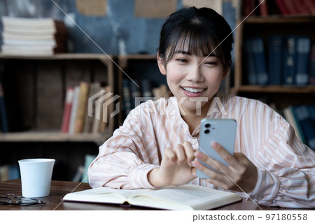 Young woman operating a smartphone while reading Young woman operating a smartphone while reading 97180558