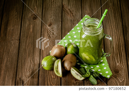 Front view of green smoothie in glass jar with straw and ingredients on wooden background. Good food Front view of green smoothie in glass jar with straw and ingredients on wooden background. Good food 97180652