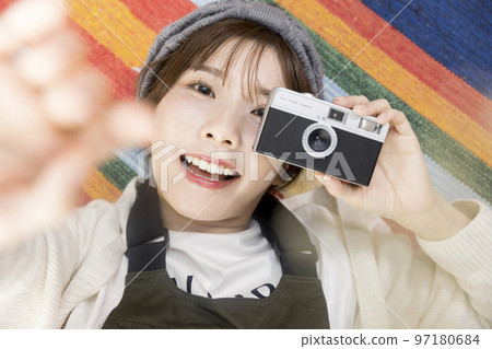 年輕女子躺在地毯上,拿著膠卷相機 年輕女子躺在地毯上,拿著膠卷相機 97180684