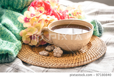 Home composition with a cup of tea, flowers and a knitted element in the bed. 97180840