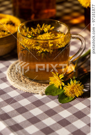 Dandelion flower healthy tea in glass teapot and glass cup on table. Delicious herbal Hot tea from fresh dandelion flowers at home at summer day. Green clearing. Bouquet of dandelions petals 97181877