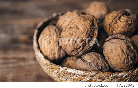 Close-up, whole walnuts in a wicker bowl on a wooden background. 97182042