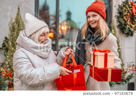 Cheerful two women are having fun in the city street at the Christmas time, laughing and buying presents for their darlings. Consumerism, shopping, lifestyle concept. Cheerful two women are having fun in the city street at the Christmas time, laughing and buying presents for their darlings. Consumerism, shopping, lifestyle concept. 97183679