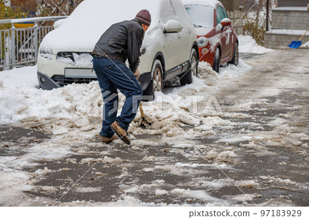 A man removes snow and ice stuck to the road with a shovel from the sidewalk. A man removes snow and ice stuck to the road with a shovel from the sidewalk. 97183929