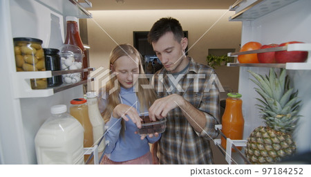 Brother and sister open the refrigerator and eat candy. Snacking junk food 97184252