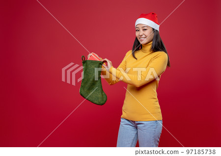 Smiling and excited young woman in santa hat putting gifts into stocking 97185738