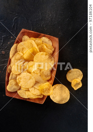 Potato chips in a wooden bowl, salty crisps, shot from the top on black Potato chips in a wooden bowl, salty crisps, shot from the top on black 97186104