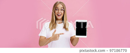 Girl suggests buy digital tablet for university and forget paper books. Excited happy and delighted young female student in white t-shirt and glasses pointing at device screen recommending gadget 97186770