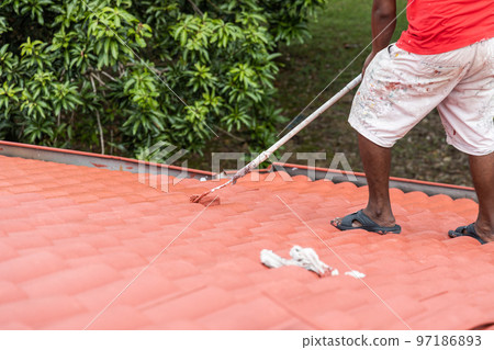 Worker painting red rooftop with roller at residential building during renovation Worker painting red rooftop with roller at residential building during renovation 97186893