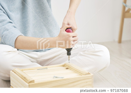 Close-up of a woman doing DIY indoors with an electric screwdriver Close-up of a woman doing DIY indoors with an electric screwdriver 97187088