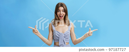 Amazed and surprised charismatic attractive woman raising hands pointing sideways left and right with impressed overwhelmed expression, smiling broadly liking both sides of copy space over blue wall Amazed and surprised charismatic attractive woman raising hands pointing sideways left and right with impressed overwhelmed expression, smiling broadly liking both sides of copy space over blue wall 97187727