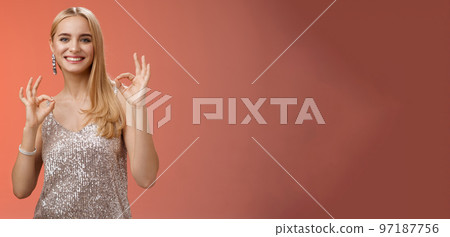 No problem friend. Charming carefree tender blond european woman in silver dress show okay ok gesture smiling pleased recommend awesome party assure having fun, feel excellent red background 97187756