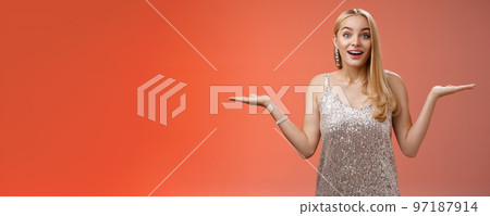 Carefree fascinated young blond girl 20s in silver glittering evening party dress raising hands sideways weighing shrugging smiling amused search right choice, deciding what do red background Carefree fascinated young blond girl 20s in silver glittering evening party dress raising hands sideways weighing shrugging smiling amused search right choice, deciding what do red background 97187914