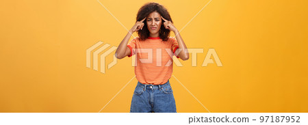 Girl cannot concentrate and think straight being loaded with bad thoughts looking concerned and intense, frowning holding fingers on temples suffering disorientation and migraine over orange wall Girl cannot concentrate and think straight being loaded with bad thoughts looking concerned and intense, frowning holding fingers on temples suffering disorientation and migraine over orange wall 97187952