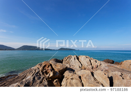Summer seashore Amazing sea clear blue sky and white clouds Wave crashing on seashore with rocks in the foreground 97188186