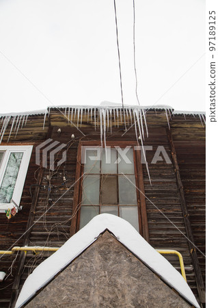 Icy, multiple icicles hang on the edge of the roof, winter or spring. 97189125