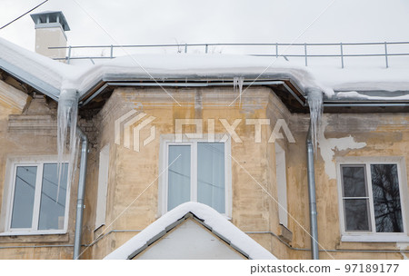 Long, frozen icicles hang on a drainpipe, spring or winter 97189177
