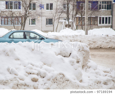 Large snowdrifts against the backdrop of a city street with a car. Large snowdrifts against the backdrop of a city street with a car. 97189194