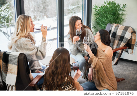 Young women enjoying winter weekends inside contemporary barn house. Four girls having fun and drinking red wine. 97191076