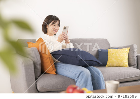 坐在沙發上看智能手機的女人 坐在沙發上看智能手機的女人 97192599