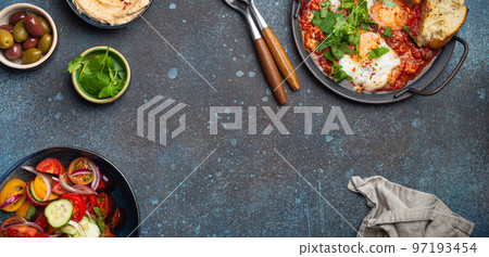 Middle Eastern breakfast or brunch with Shakshouka, toasts, vegetables salad, hummus, olives copy space 97193454