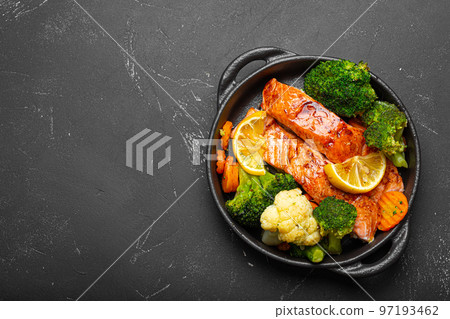 Healthy baked fish salmon steaks, broccoli, cauliflower, carrot in cast iron casserole bowl on black dark stone background. Cooking a delicious low carb dinner, healthy nutrition 97193462