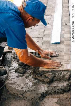 Bricklayer lays tiles. Professional builder in overalls and baseball cap at work. Elderly mason 97193469