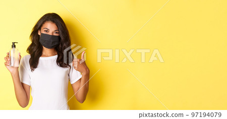 Concept of covid-19, social distancing and lifestyle. Portrait of cheerful african-american girl in face mask, recommend to use antiseptic, showing hand sanitizer and thumbs-up Concept of covid-19, social distancing and lifestyle. Portrait of cheerful african-american girl in face mask, recommend to use antiseptic, showing hand sanitizer and thumbs-up 97194079