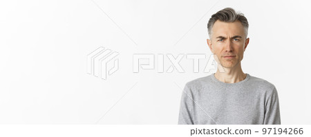 Close-up of skeptical middle-aged man, frowning and looking doubtful at camera, standing over white background in gray sweater 97194266