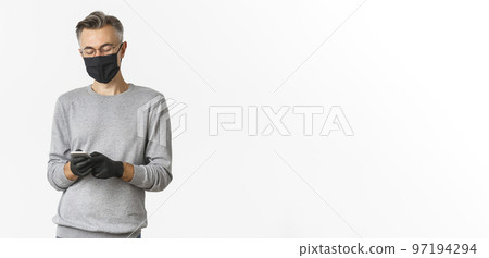 Concept of covid-19, social distancing and lifestyle. Image of handsome middle-aged man in glasses, medical mask and gloves, using mobile phone, messaging or browsing social network Concept of covid-19, social distancing and lifestyle. Image of handsome middle-aged man in glasses, medical mask and gloves, using mobile phone, messaging or browsing social network 97194294