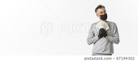 Concept of covid-19, social distancing and lifestyle. Portrait of cheerful rich man in medical mask, gloves and glasses, bragging with money and looking pleased, winning lottery 97194302
