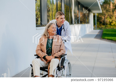 Young woman doctor taking care of senior woman at wheelchair. 97195066