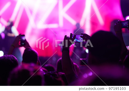 Hand with a phone records live music festival. People taking photographs with smart phone during concert. 97195103